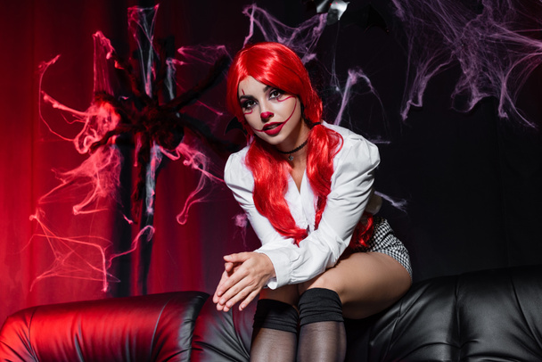 roodharige vrouw in clown make-up kijken naar camera op donkere achtergrond met spinnenweb - Foto, afbeelding