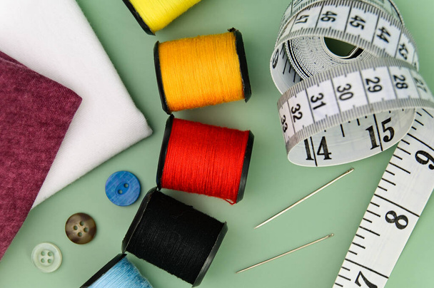 Sewing accessories and fabric on a green background. Including needle, thread, buttons and measuring tape. - Photo, Image