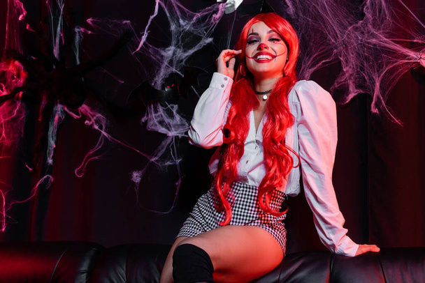 vrolijk roodharige vrouw in clown make-up op zwarte achtergrond met spinnenweb - Foto, afbeelding