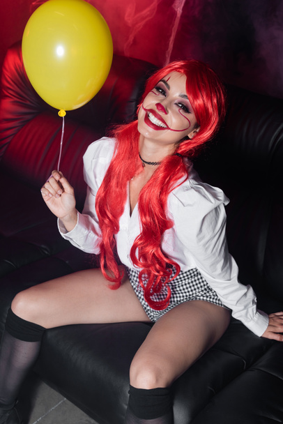 vista ad alto angolo di eccitata rossa donna con palloncino giallo e trucco di Halloween su sfondo scuro - Foto, immagini