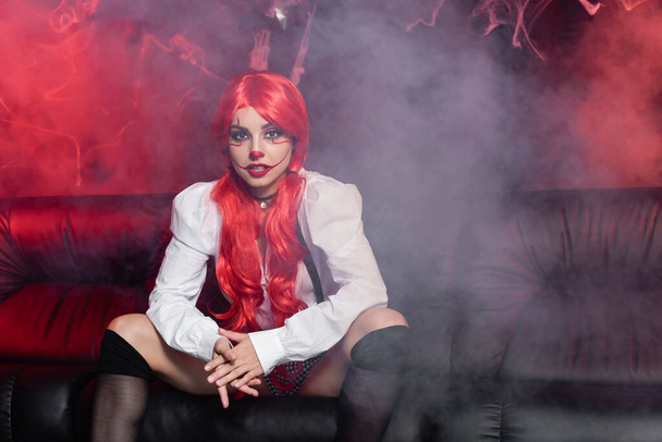 woman with red hear and halloween makeup looking at camera near fog on dark background - Photo, Image