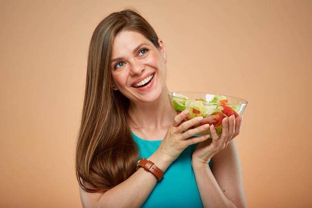 glimlachende vrouw met salade glazen schaal omhoog kijkend, geïsoleerd portret op geel bruine achtergrond. - Foto, afbeelding