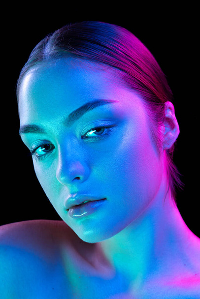 Closeup young beautiful woman with well-kept skin and sophisticated facial features isolated over dark background in purple neon light. Concept of art, fashion, style, inspiration, emotions. - Fotoğraf, Görsel