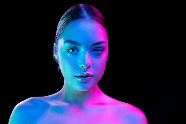 Perfection. Beauty portrait of young adorable woman with well-kept skin isolated over dark background in purple neon light. Concept of art, fashion, style, inspiration, emotions. Copy space for ad - Foto, imagen