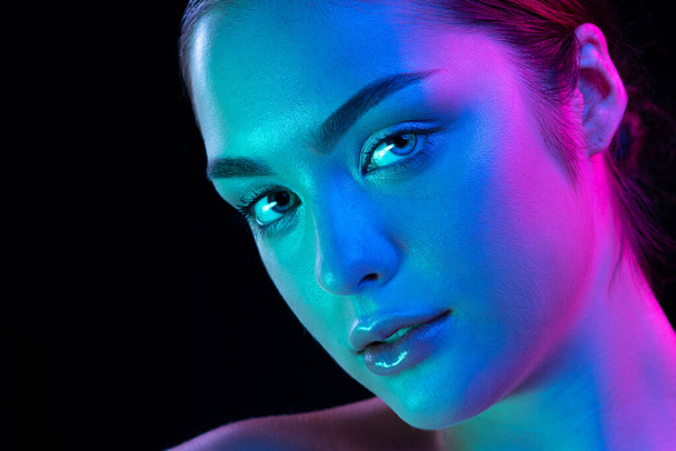 Closeup young beautiful woman with well-kept skin and sophisticated facial features isolated over dark background in purple neon light. Concept of art, fashion, style, inspiration, emotions. - Фото, зображення