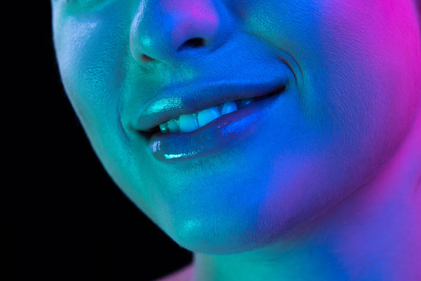 Smile. Closeup female lips, cheeks and nose isolated over dark background in neon light. Natural beauty. Concept of natural beauty, cosmetology, skincare, cosmetics, plastic surgery, ad - Fotografie, Obrázek