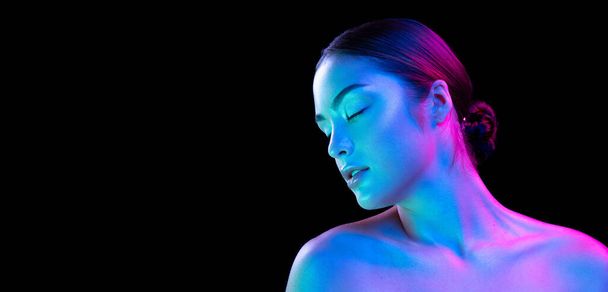 Charm, flirt. Young beautiful girl with well-kept skin and without makeup isolated over dark background in neon light. Concept of natural beauty, art, emotions, cosmetics and youth. Flyer for ad - 写真・画像