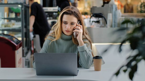 Serious business woman freelance manager worker student sitting at table with laptop answering call talking on phone angry arguing with colleagues problems misunderstanding drinks coffee multitasking - Foto, Imagen
