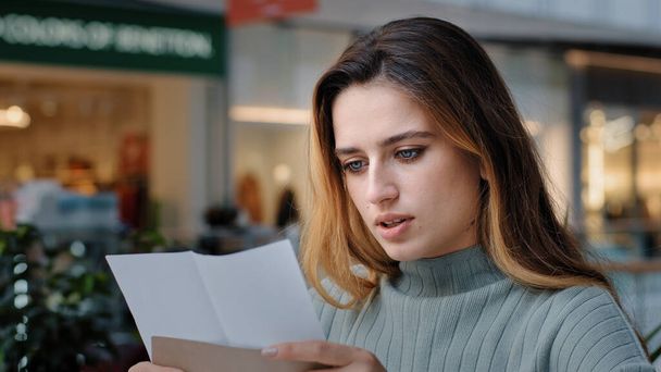 Portrait of beautiful young caucasian millennial woman recipient girl sitting in cafe receiving letter opens envelope reads test results bank notice news from friends new job offer insurance statement - Photo, Image