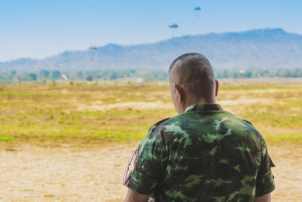 Обратный вид на азиатских солдат армии стоит, чтобы исследовать ландшафт в поле. Солдат командного класса стоит, чтобы наблюдать и проверять условия маневра на открытой местности с парашютом на заднем плане. - Фото, изображение
