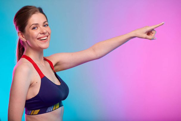 Smiling sporty woman in fitness sportswear pointing finger to empty space. Female fitness portrait isolated on neon multicolor background. - Fotó, kép