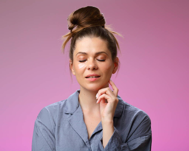 Woman pajama dressed with closed eyes, isolated on pink, female face portrait with under eyes patches and bun hair. - Photo, image