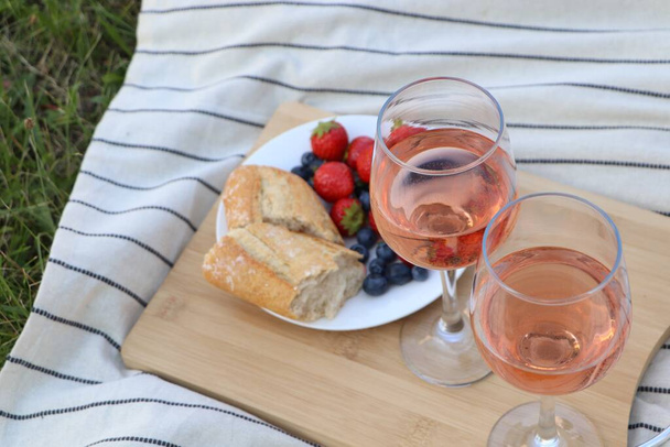 Glasses of delicious rose wine and food on picnic blanket outdoors - Фото, зображення