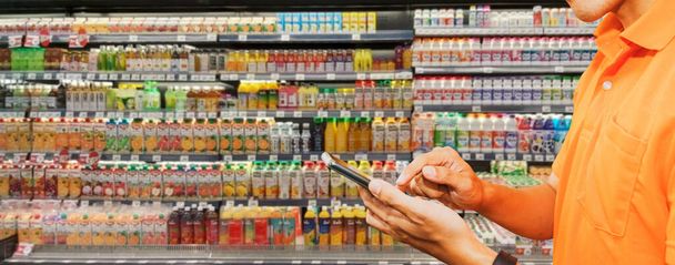 Entre bastidores trabaja un repartidor de comida con smartphone que recibe pedidos de clientes que ordenan comida en el supermercado comprando productos de calidad de jugo en el supermercado en línea. - Foto, imagen