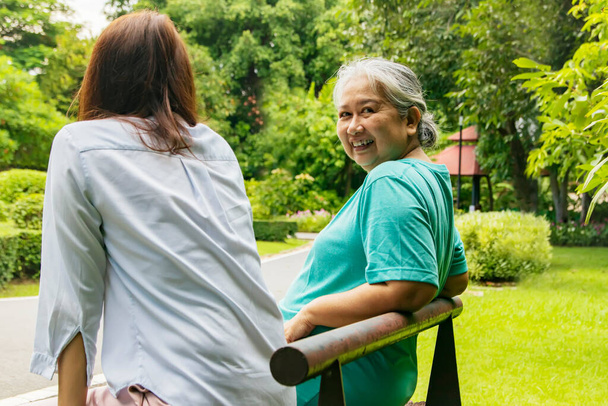 Emekli Asyalı son sınıf öğrencisi bir kadın kızı ile birlikte bahçede oturuyor. Spor yaptıktan sonra rahatlamak ve sağlıklı bir şekilde kameraya bakarken egzersiz yapmak için.. - Fotoğraf, Görsel