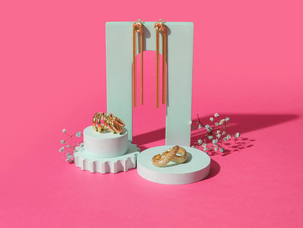 Showcase pedestals with trendy earrings and gypsophila flowers on pink background - 写真・画像