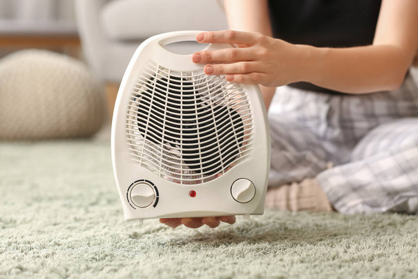 Woman with electric fan heater sitting on carpet at home, closeup - Foto, immagini