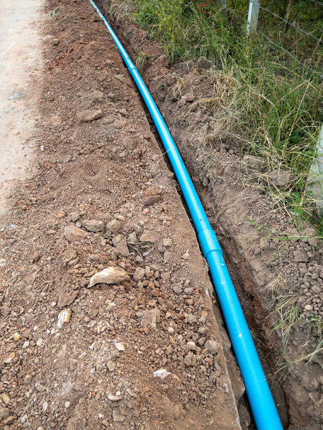 Uusi PVC-putki on makaa kaivannon pitkin betonitietä vesihuollon maaseudun kylässä, edessä näkymä kopio tilaa. - Valokuva, kuva