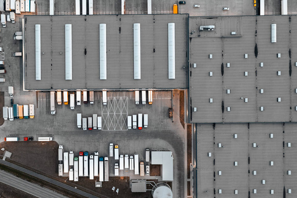 Вид с воздуха на склад с товарами. Логистический центр в индустриальной зоне города, многие грузовики ждут погрузки на логистический склад - Фото, изображение