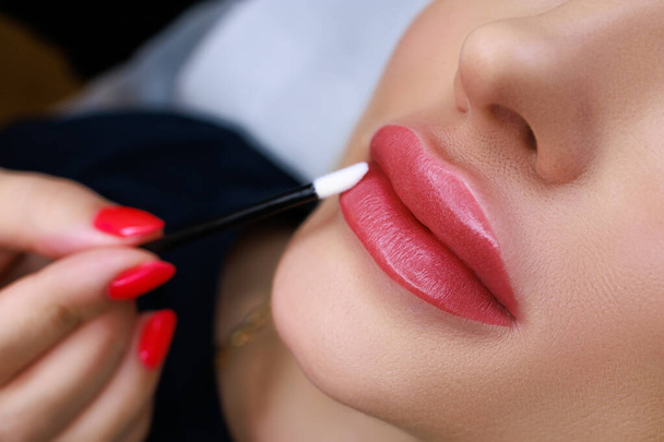 close-up of the model's lips with permanent make-up, the master wipes the model's lips with a cotton swab - Φωτογραφία, εικόνα