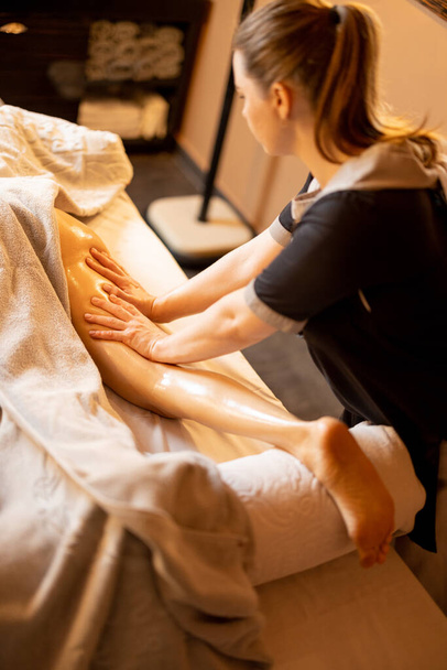 Woman receiving professional recovering and anti-cellulite massage on her legs at Spa salon. Client lying covered with towel on medical couch, close-up on leg - Foto, Imagen
