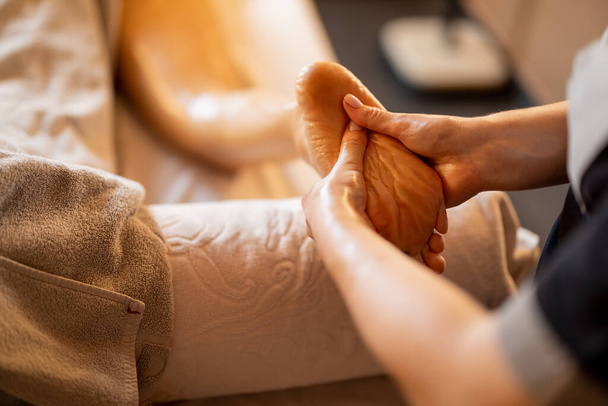 Woman receiving professional relaxation massage on her foot at Spa salon. Client lying covered with towel on medical couch, close-up on leg - Foto, Bild
