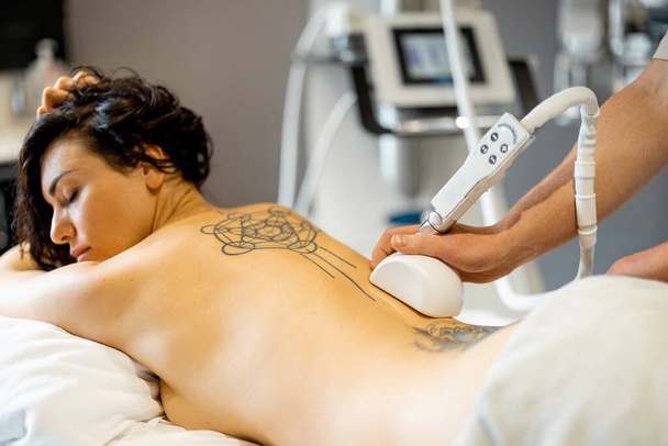 Woman receiving vacuum roller massage on her back at medical beauty centre. Lymphatic drainage massage procedure. Womans back with tattoos - Фото, изображение