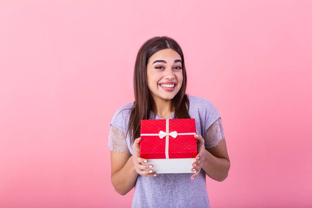Весела красива молода жінка тримає червону подарункову коробку в руках, на рожевому тлі. Концепт свята та подарунки
 - Фото, зображення