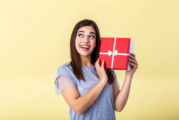 Portrait of young lovely nice sweet glamorous girl lady, wearing gray top, carrying gift box, wondering about surprise. Isolated over bright vivid yellow background - Foto, Imagem