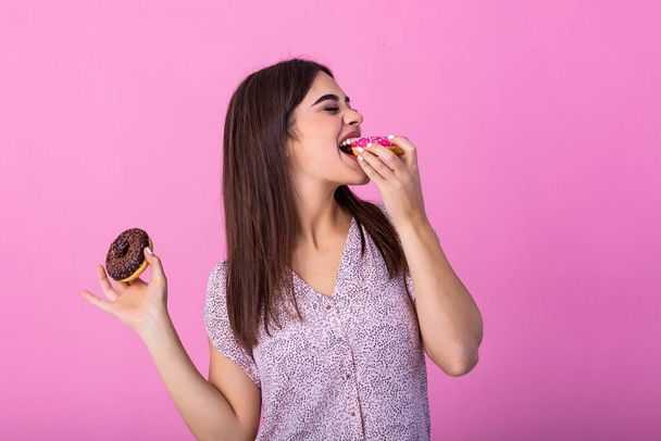 Beauty model girl eating colorful donuts. Funny joyful Vogue styled woman choosing sweets on pink background. Diet, dieting concept. Junk food, Slimming, weight loss - Foto, afbeelding