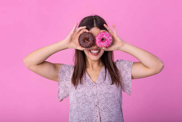 Close up portrait of a cute girl posing with donuts at her face isolated over violet background. Beautiful woman with donuts on her eyes - Foto, Bild
