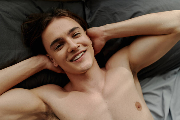 top view of man lying on bed with hands behind head and smiling at camera - Fotoğraf, Görsel