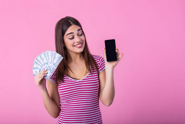 Excited attractive woman holding smartphone and money, cashback. Image of excited young lady isolated over pink background. Showing display of mobile phone holding money. - Fotoğraf, Görsel