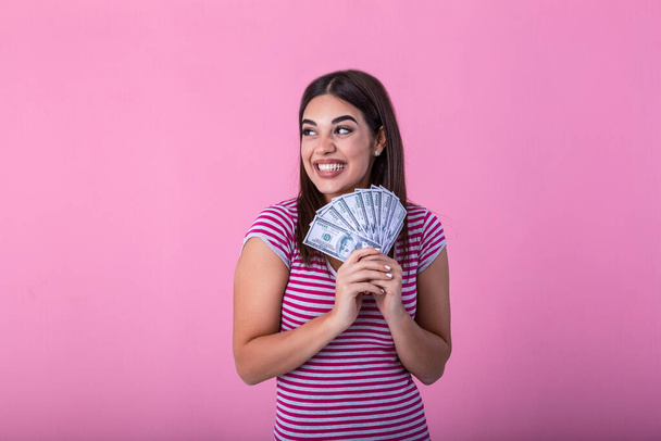 Portrait of nice amazed wondered attractive cheerful positive lady wearing striped pullover holding money in hands showing fan of hundreds isolated over bright vivid pink background - Foto, imagen