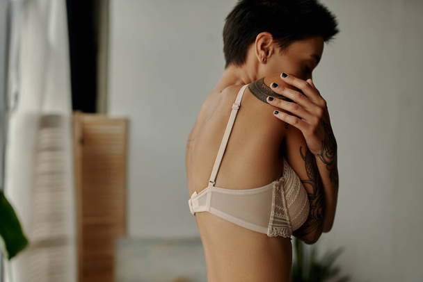 side view of brunette woman in beige bra embracing herself in bedroom - Foto, Imagem