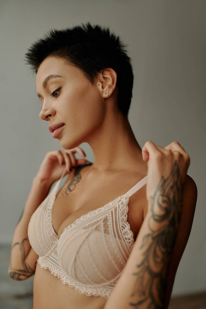 Sexy tattooed woman touching bra straps at home  - Фото, изображение