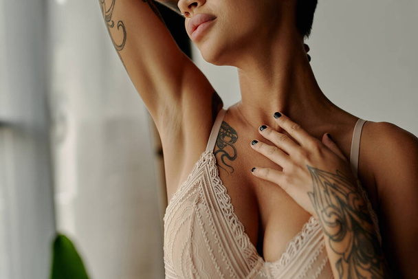 Vue recadrée d'une femme tatouée en soutien-gorge en dentelle touchant la poitrine à la maison  - Photo, image