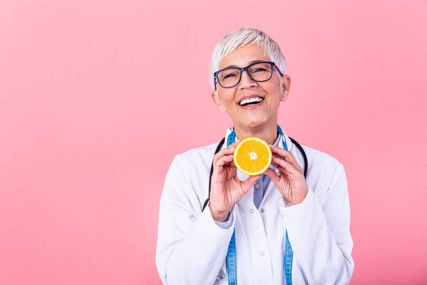 Dietician holding an orange. Smiling nutritionist holding a sliced orange, vitamins and healthy diet concept. Good medical healthcare nutrition concept. - Photo, image