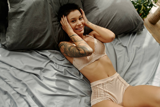 Hoge hoek uitzicht van glimlachende vrouw in lingerie liggend op bed thuis  - Foto, afbeelding