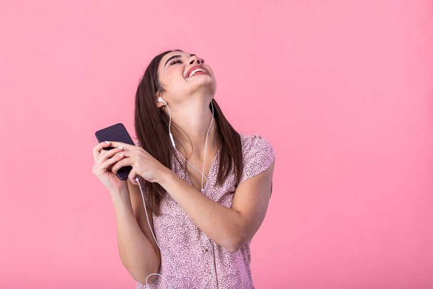 Концепція способу життя - Портрет красивої жінки, що радісно слухає музику з навушниками на мобільному телефоні. Рожевий пастельний студійний фон. Копіювати пробіл
. - Фото, зображення