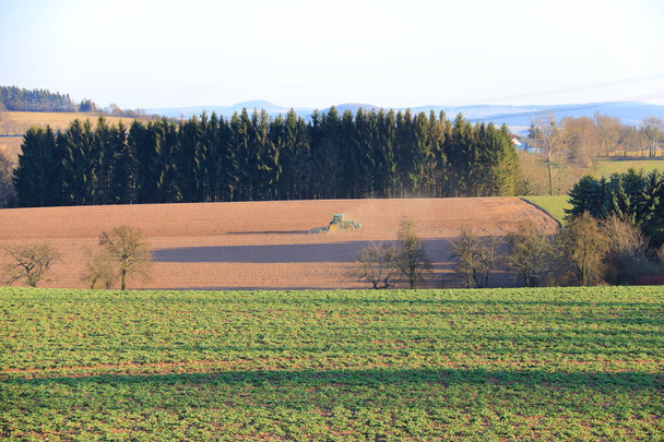 April 7 2018 - Saxony, Germany: Tractor working on the farm, a modern agricultural transport, a farmer working in the field, fertile land, tractor on sunset background, cultivation of land, agricultural machine - Zdjęcie, obraz