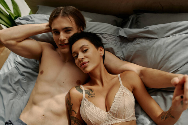Вид зверху молода сексуальна пара тримає руки і дивиться на камеру на ліжку
  - Фото, зображення