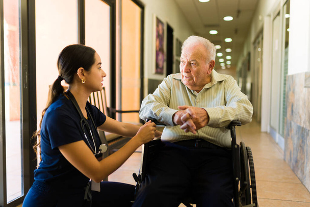 Loving patient nurse comforting while talking with a elder mature man in his 80s on a wheelchair staying at the nursing home - Foto, immagini