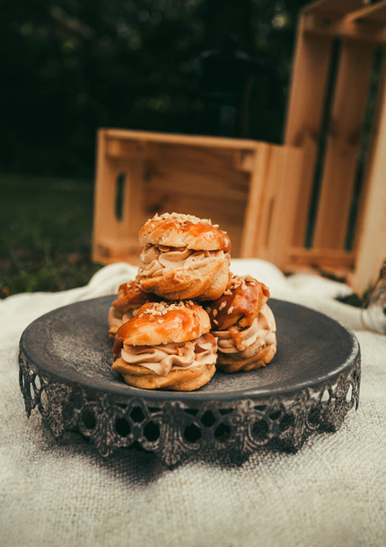 Picnic in nature - tasty Profiterole cakes with park on background. Delicious cakes on the grey plate in nature. - 写真・画像