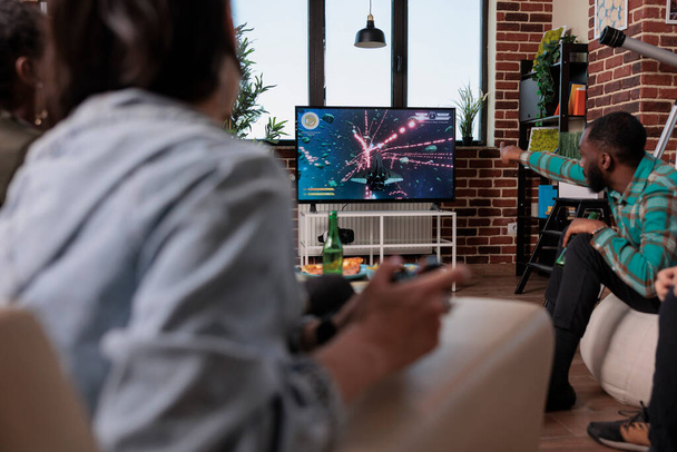 Group of men and women having fun with shooter video games on tv, using console to play on television. Playing shooting game at social gathering with friends, enjoying leisure activity and gaming. - Foto, imagen