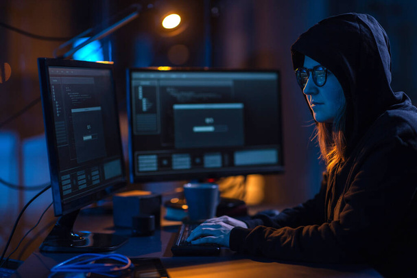 cybercrime, hacking and technology concept - female hacker in dark room writing code or using computer virus program for cyber attack - Fotografie, Obrázek