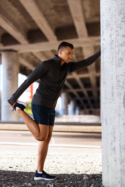 fitness, sport and healthy lifestyle concept - man stretching leg under bridge - Photo, Image