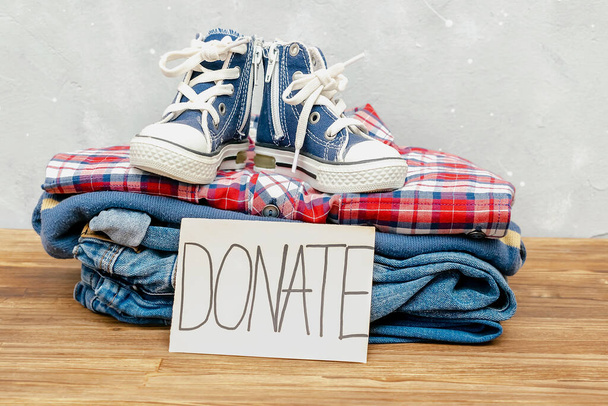 Stack of old baby children clothes,sneakers shoes sorted into Donate categories.Donation,volunteering help,humanitarian aid.charity on gray background still life.Recycle clothing,eco cotton. - Photo, Image