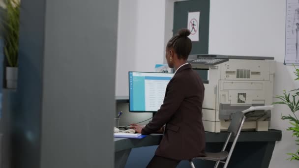 Medical worker answering landline phone call at reception desk counter, having remote conversation on cord telephone. Receptionist working on checkup appointments with computer in facility lobby. - Πλάνα, βίντεο