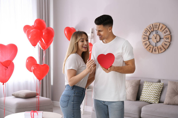Man presenting gift to his girlfriend in room decorated with heart shaped balloons. Valentine's day celebration - Foto, Imagem
